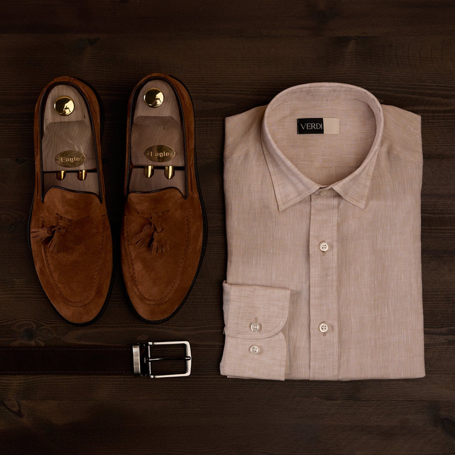 Brown loafers, belt, and light brown shirt on a wooden surface